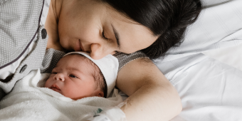 Eine Mama kuschelt nach der Geburt liebevoll mit ihrem Neugeborenen im Kreißsaal. Die NAse der Mutter leigt auf der Stirn des wachen Kindes.