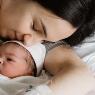 Eine Mama kuschelt nach der Geburt liebevoll mit ihrem Neugeborenen im Kreißsaal. Die NAse der Mutter leigt auf der Stirn des wachen Kindes.