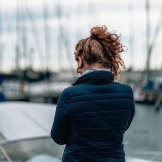 Frau steht auf einem Anleger, im Hintergrund sind Segelboote zu sehen. 